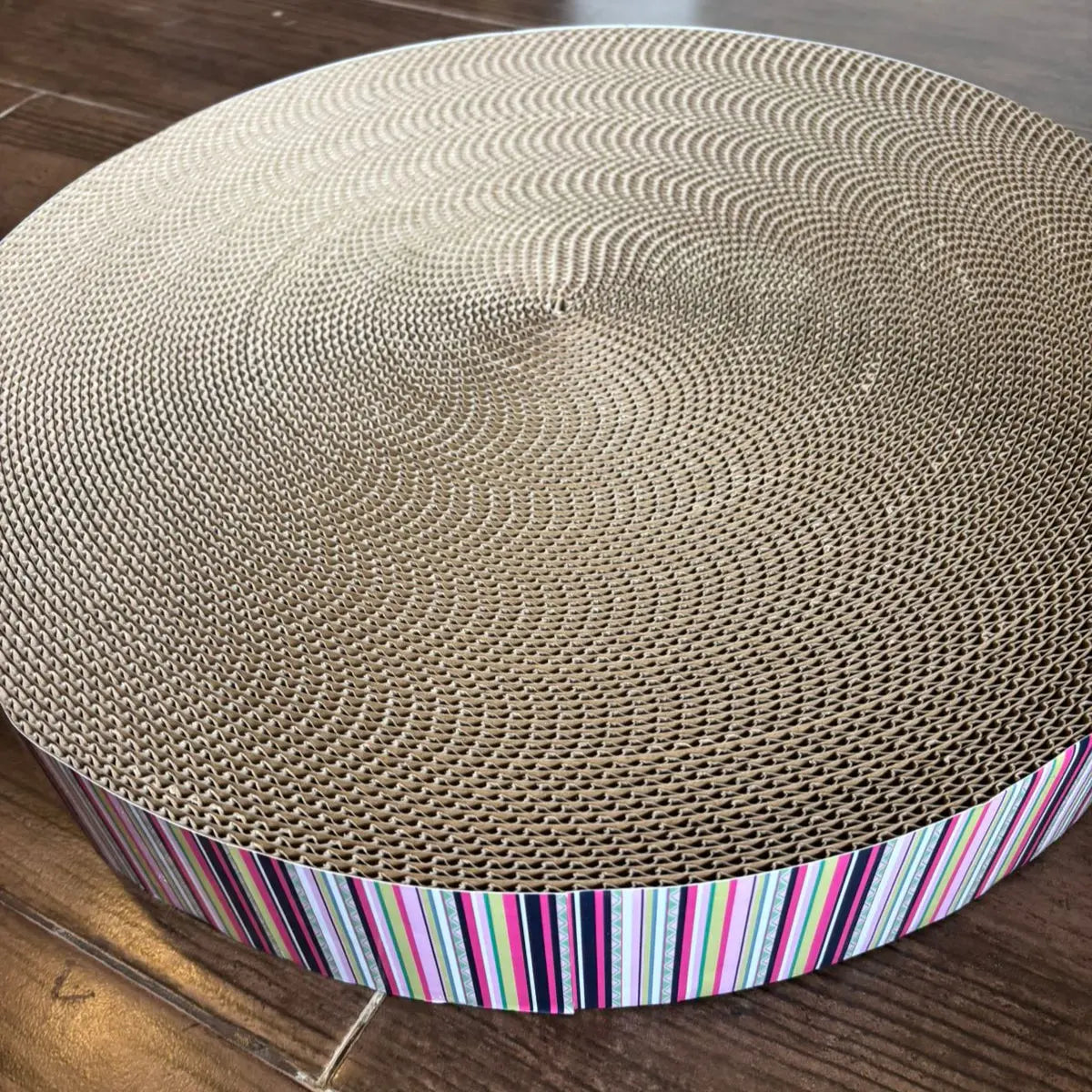 Round cardboard cat scratcher with striped base on a wooden floor