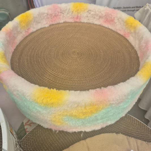 Round cat bed with colorful fleece exterior and brown sisal center on a surface.