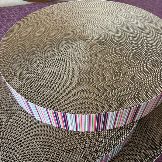 Round cardboard scratcher with a colorful striped band on a purple surface
